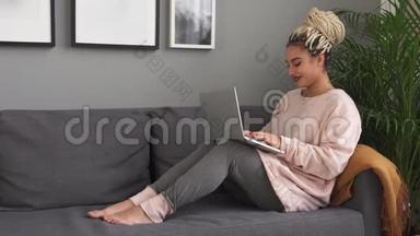 年轻漂亮的女人坐在家里的<strong>现代沙发</strong>上用笔记本电脑工作